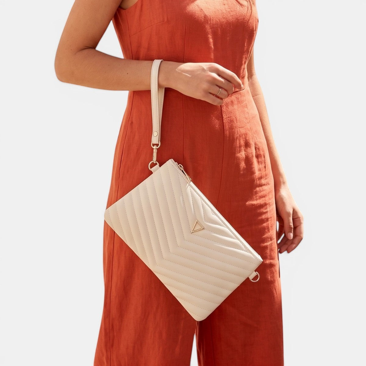 Lederax cream quilted faux leather clutch bag with V-stitch detail and gold hardware, held by a wrist strap.